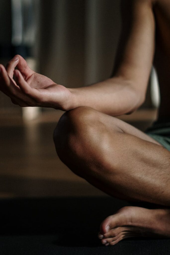 A shirtless man in a yoga studio meditating in the lotus position for relaxation and wellness.